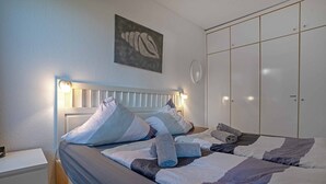 A bedroom with a bed, pillows, a bedside table, a wall-mounted artwork, and a wardrobe.
