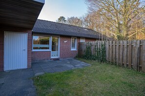 En boligbygning med facade af mursten, en hvid dør og en lille forhave med et træhegn.
