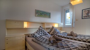 A bedroom with two beds, wooden headboards, a window with curtains, and a painting on the wall.
