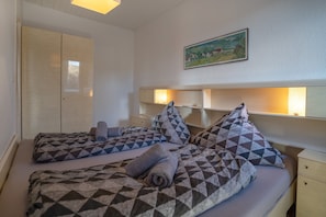 Et hotelværelse med to senge, et garderobeskab, et billede på væggen og sengeborde med lamper.