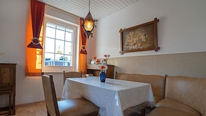 A dining area with a table, chairs, a vase of flowers, a painting, and a window with curtains.