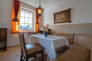 Et spiseområde med et bord, stole, en vase med blomster, et maleri og et vindue med gardiner.