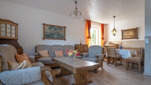A living room with a wooden coffee table, multiple sofas, and chairs. There is a painting on the wall and a chandelier.