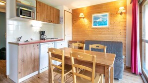 A compact kitchen with wooden cabinets, a microwave, and a dining area with a table and chairs. - Cozy Ski Retreat in Chamrousse (Chamrousse)