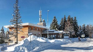 A building with a wooden facade, a sign for 'Bachat', and a snow-covered landscape with trees. - Cozy Ski Retreat in Chamrousse (Chamrousse)