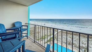 A balcony with blue Adirondack chairs overlooking a beach with a pool. - Island Winds East 608 | Walk to the HangOut! | Beachfront | Pool | My Beach Getaways (Gulf Shores)
