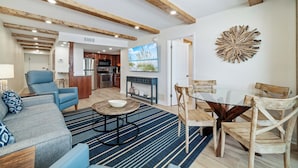 A spacious living area with a sofa, chairs, a coffee table, and a TV. - Island Winds East 608 | Walk to the HangOut! | Beachfront | Pool | My Beach Getaways (Gulf Shores)