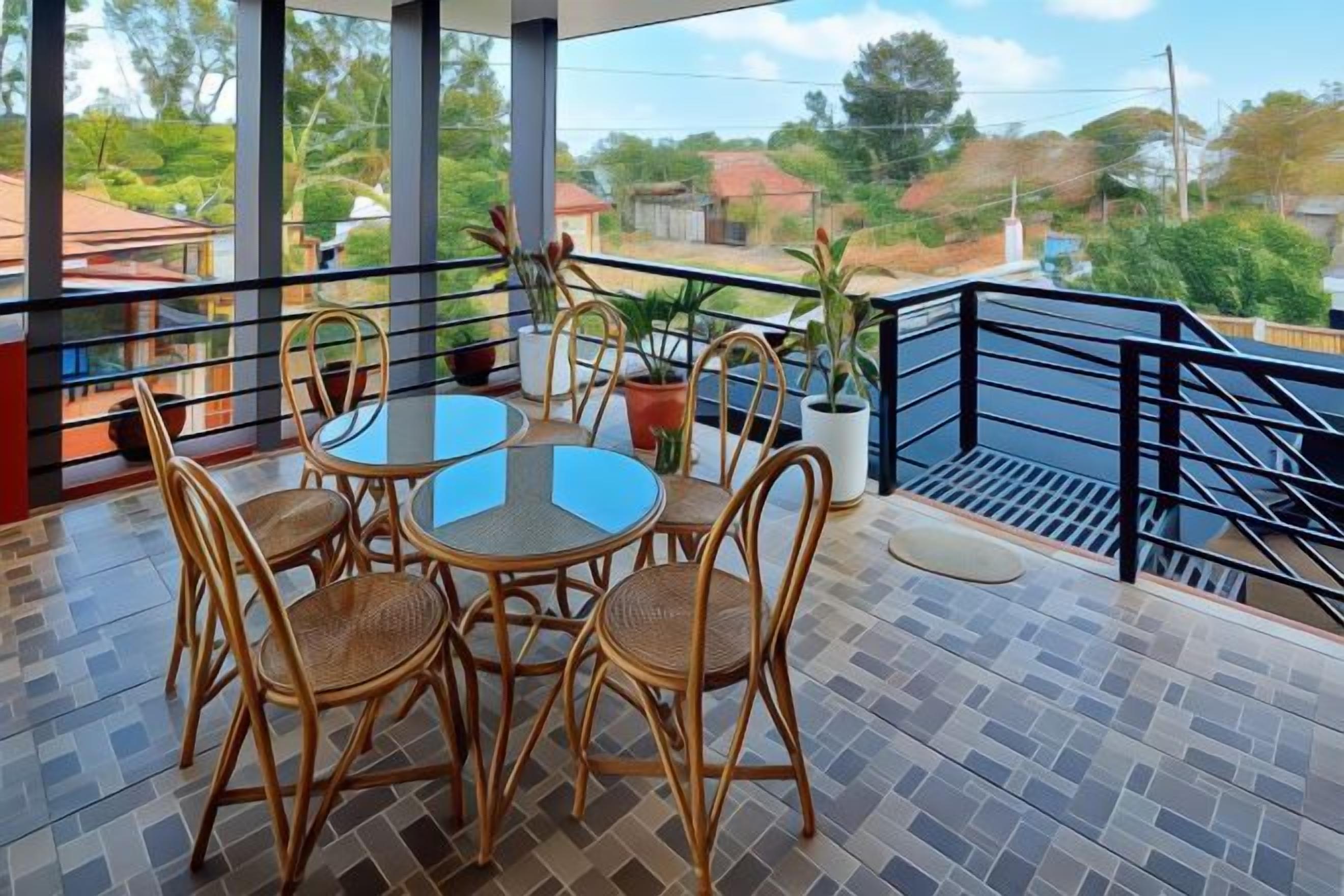 A balcony with a table and chairs, potted plants, and a view of the surrounding area.