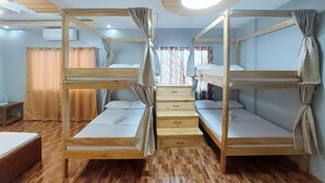 Quarto com beliches, piso de madeira, luminária no teto e janela com cortinas.