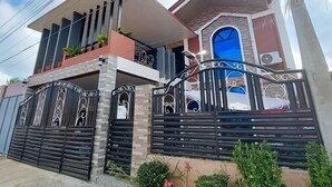 Uma casa de dois andares com varanda, entrada protegida por grades e uma janela grande.