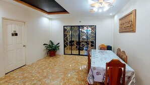 Uma sala de jantar com piso de mármore, mesa e cadeiras, uma planta em vaso e um biombo decorativo.