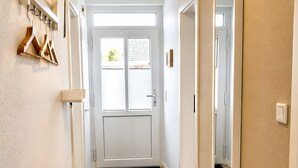 Een gang met een kapstok, een spiegel en een deur naar een kamer.