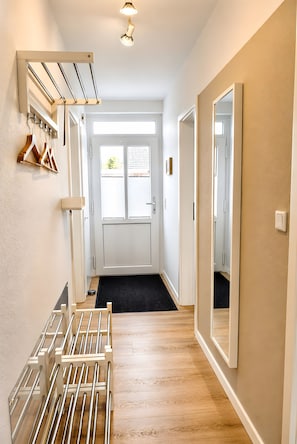 A hallway with a coat rack, a mirror, and a door leading to a room.