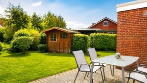 Een terras met een tafel en stoelen, een houten tuinhuis en een bakstenen muur.