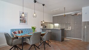 Een moderne keuken met grijze kastjes, een blauwe gestoffeerde bank en een eettafel met vier stoelen.