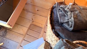 Een houten interieur met een geweven mand met een plaid, een metalen bak met stenen en een houten ladder.