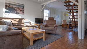 Ein Wohnzimmer mit Sofa, Sessel, Couchtisch, Fernseher und einem Bild von einer Strandlandschaft.