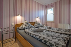 Una stanza con carta da parati a righe, un letto con copriletto decorato, un comodino e una finestra con persiane.