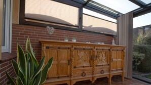 Ein Holzschrank mit aufwendigen Schnitzereien, ein Blumentopf und eine Backsteinmauer mit einem Fenster darüber.