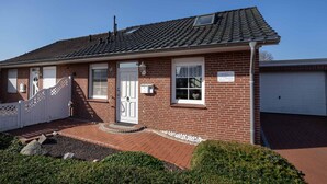 Ein eingeschossiges Ziegelhaus mit weißer Tür, einer Garage und einem kleinen Vorgarten mit weißem Zaun und Kiesweg.