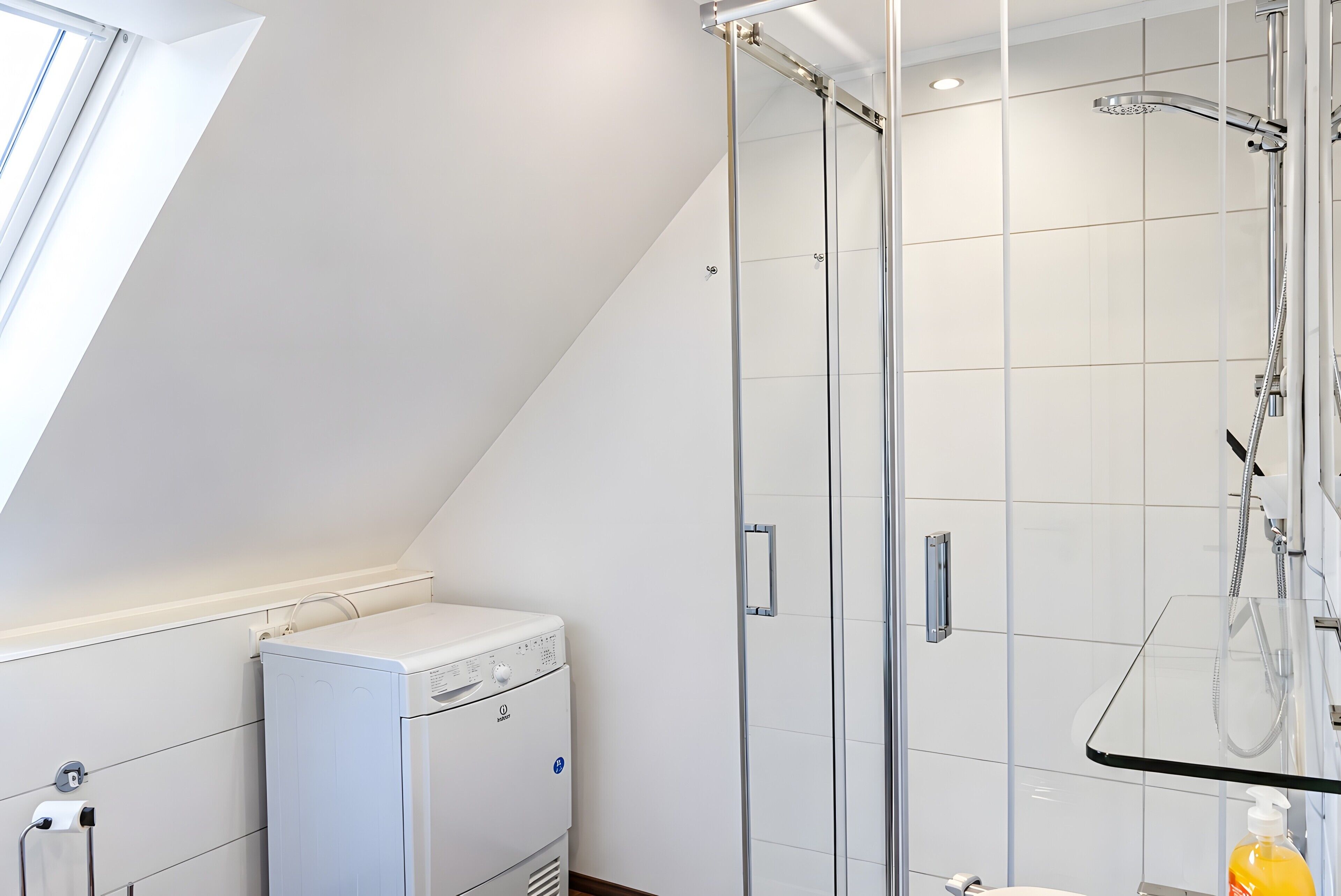 A modern bathroom with a glass shower enclosure, a built-in washing machine, and a toilet.