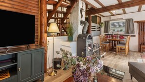 A rustic interior with a television, fireplace, dining area, and wooden beams.
