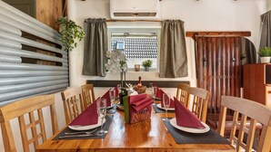 A dining area with a wooden table set for two, a potted plant, and a window with curtains.