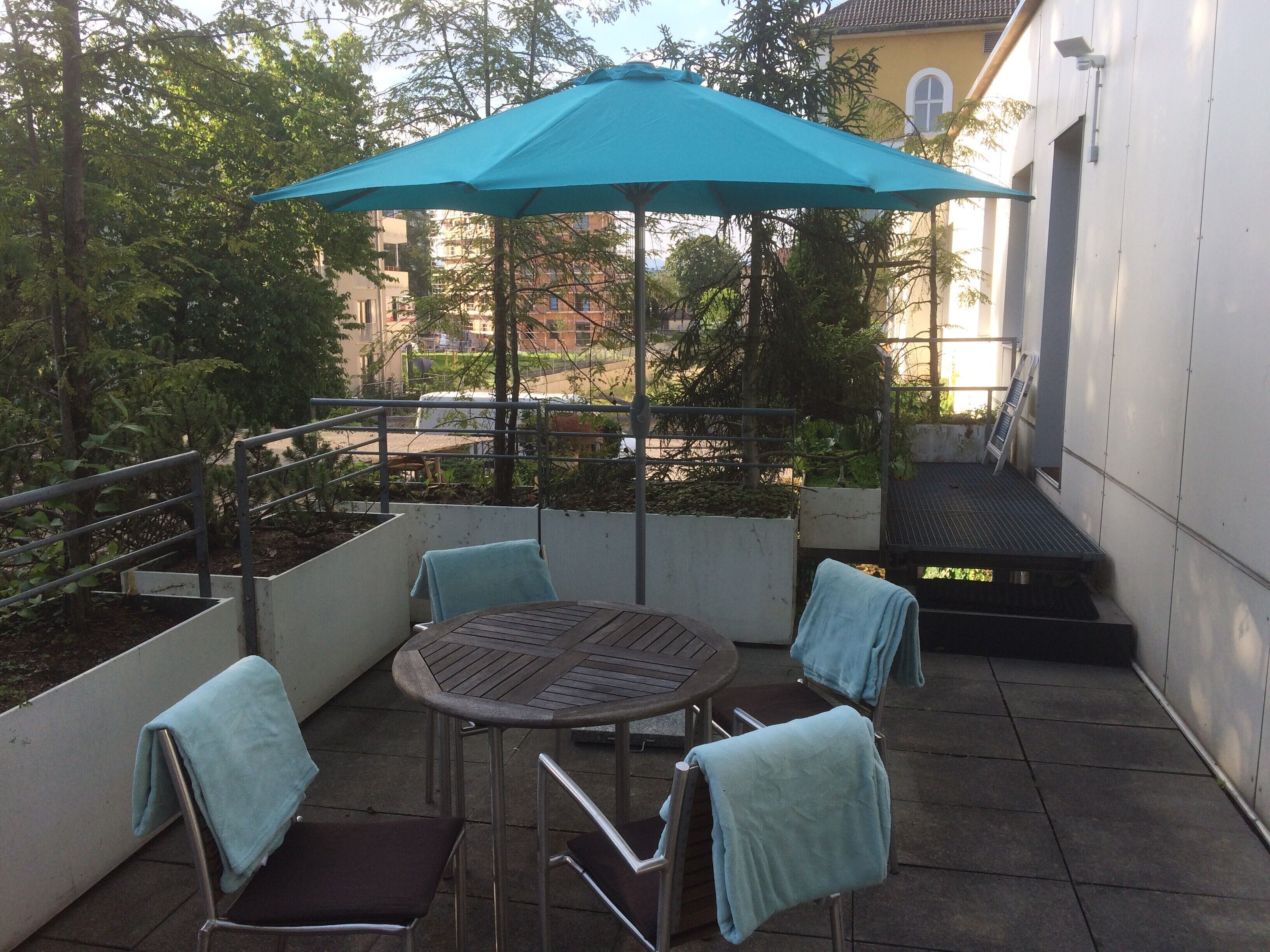 Une terrasse avec une table ronde, quatre chaises et un parasol bleu.
