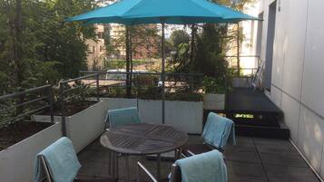 Eine Terrasse mit einem runden Tisch, vier Stühlen und einem blauen Sonnenschirm.