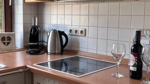 Eine Küche mit einer modernen Induktionskochplatte, einer Kaffeemaschine, einem Wasserkocher, einer Weinflasche und einem Weinglas.
