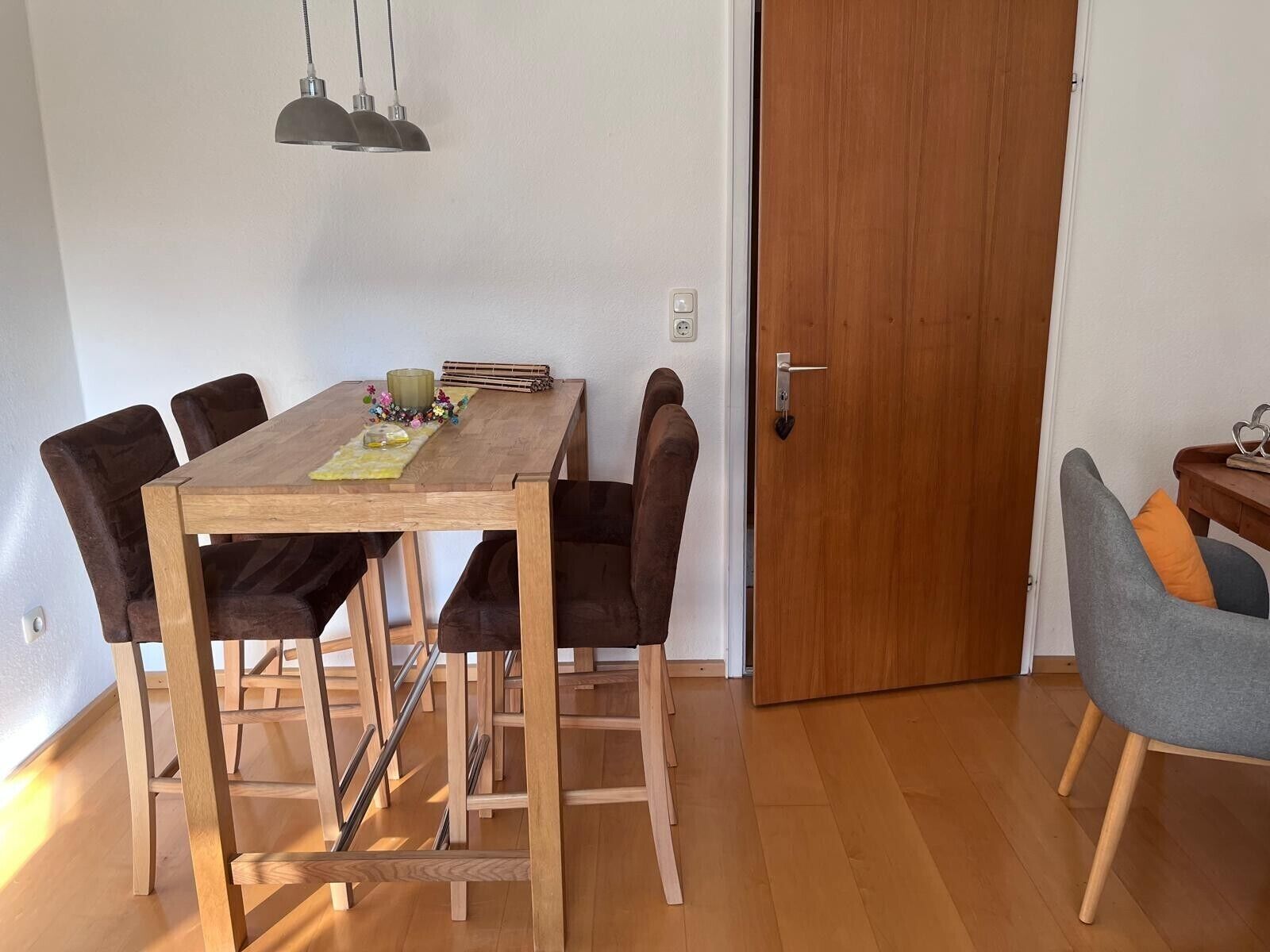 A dining area with a wooden table, six chairs, a small side table, and a door.