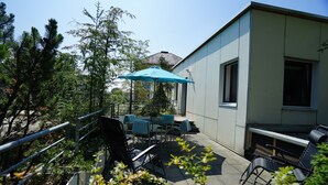Eine Terrasse im Freien mit Tisch, Stühlen und einem blauen Sonnenschirm, sowie einem Geländer.