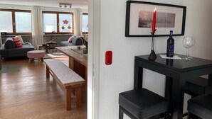 Ein Wohnzimmer mit einer Couch, einer Bank, einem Tisch, einem gerahmten Bild, einer Kerze und einer Weinflasche.