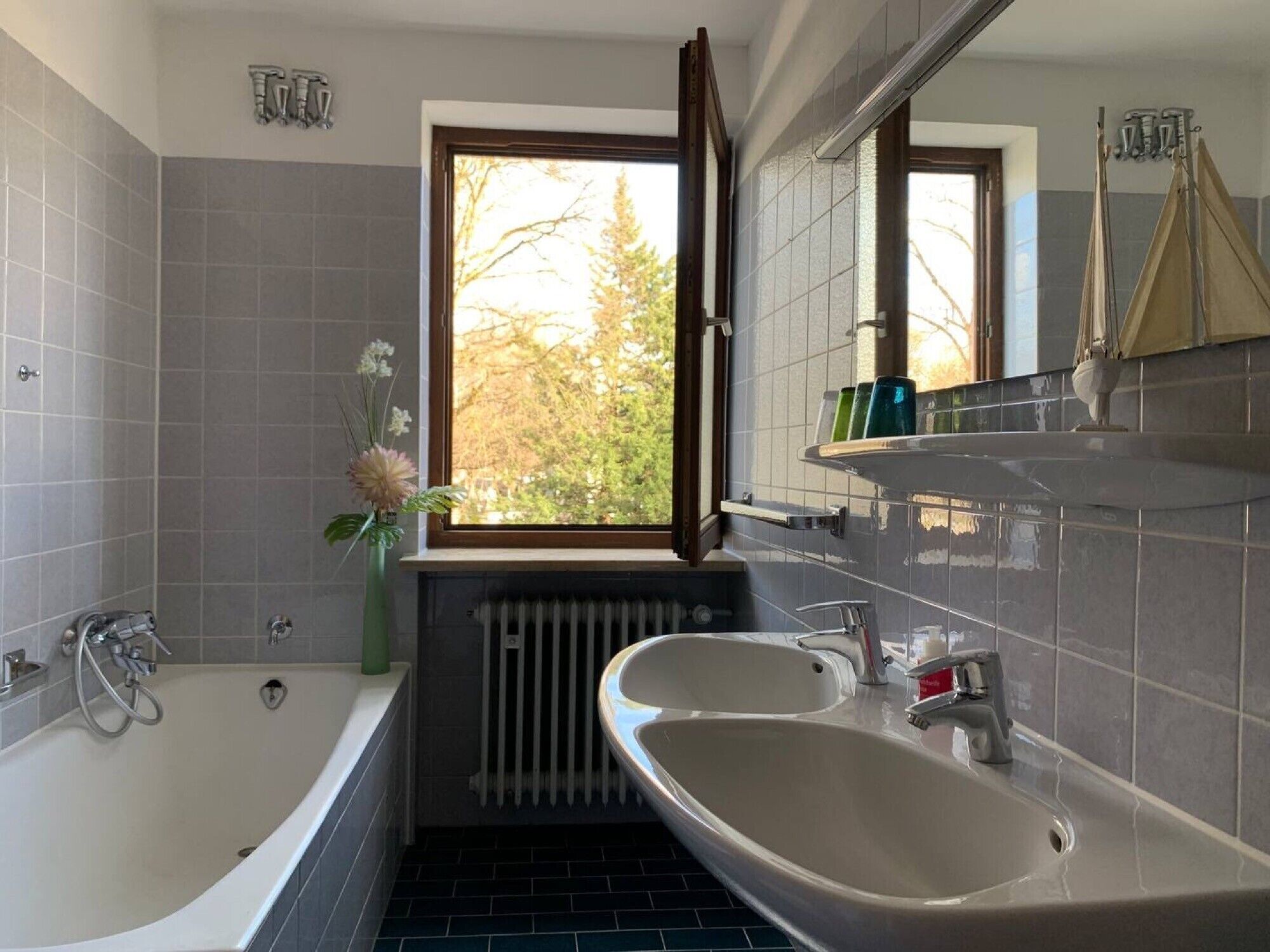 A modern bathroom with a bathtub, two sinks, a window with an open door, and a radiator.