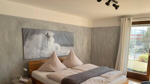 Ein Schlafzimmer mit Bett, Kissen, einem Nachttisch, einer Lampe, einem Fenster mit Vorhängen und einem Bild an der Wand.