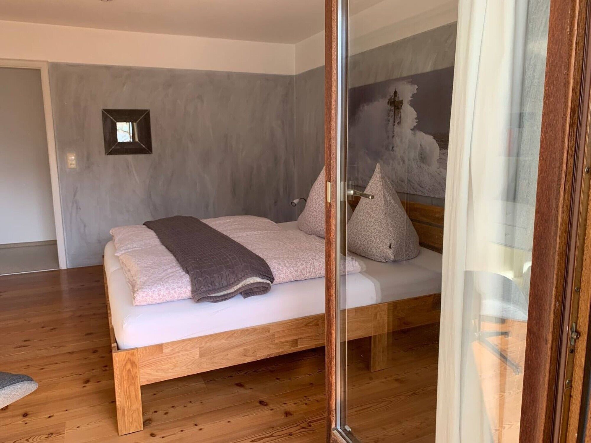 Una camera da letto moderna con un letto in legno, una porta in vetro e una parete grigia.