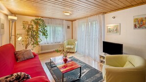 Un salon avec un canapé rouge, un fauteuil jaune, une table basse, un téléviseur et un radiateur.