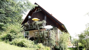 Une maison en bois dotée d’un balcon, entourée de verdure.