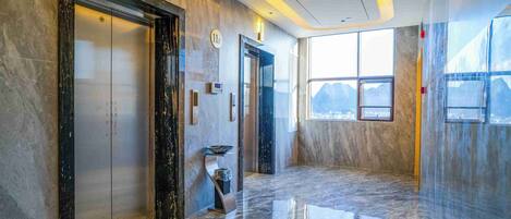 A modern elevator area with marble flooring and glass doors, a digital display, and a view of mountains through large windows.