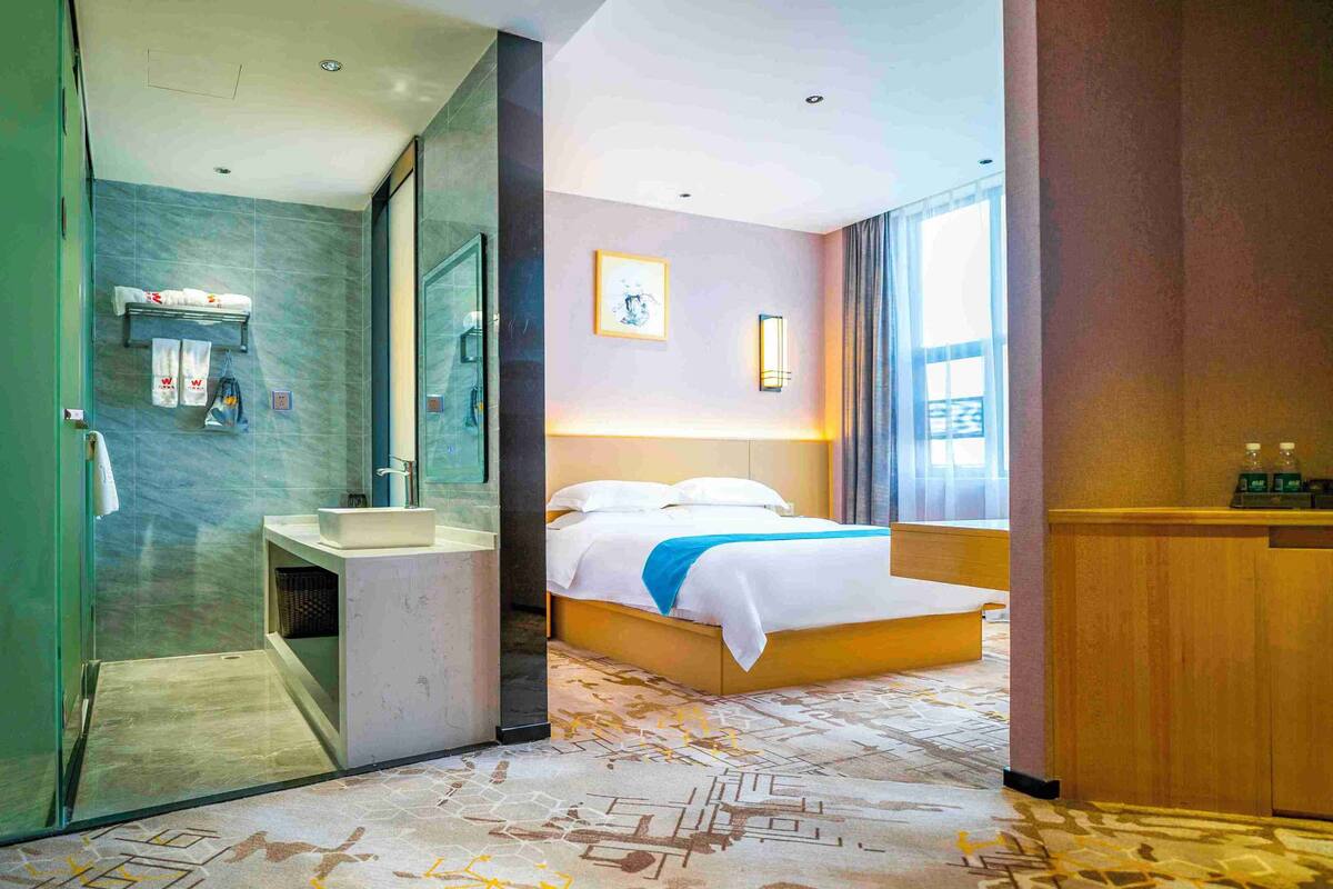 A hotel room with a bathroom, a bed, a bedside table, and a window.