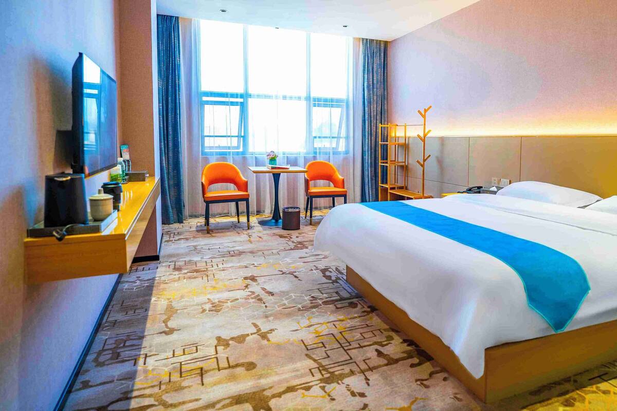 A hotel room with a large bed, a desk with a chair, a TV, and a window with curtains.