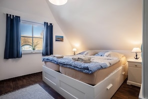 A bedroom with a bed, two bedside lamps, a window with curtains, a small potted plant, and a wall-mounted picture. - Holiday Home 'Seeschwalbe 14' with Sea View, Private Terrace and Wi-Fi (Ummanz)