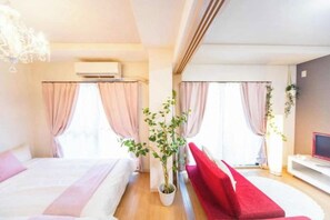 A hotel room with a bed, a red sofa, a potted plant, and a TV.