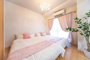 A bedroom with a bed, a chandelier, a potted plant, and a window with curtains.