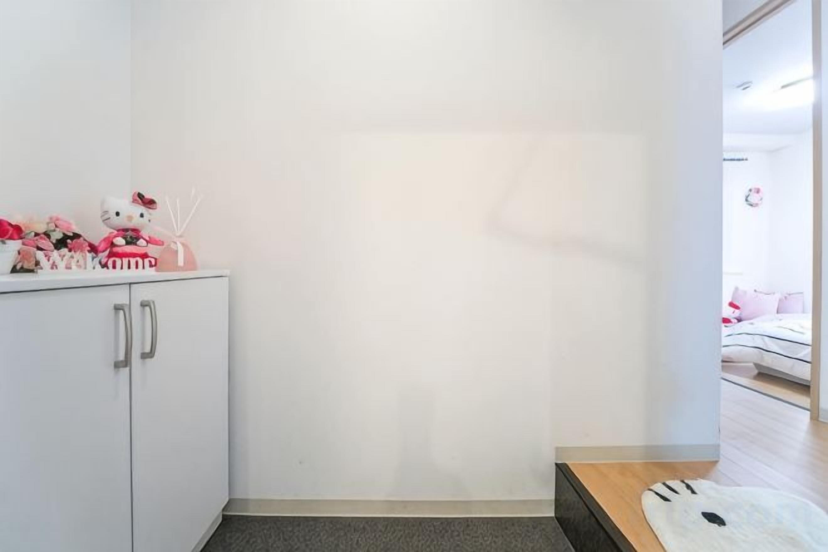 A room with a white wardrobe, a small table, and a bed with pink bedding.