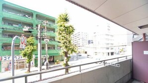 Vista desde un balcón sobre una calle con un edificio de varios pisos, un árbol y un peatón.