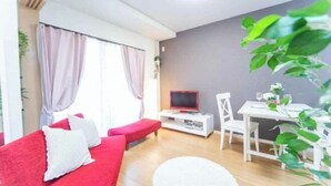 Una sala de estar con un sofá rojo, una mesa de comedor blanca y un televisor sobre un mueble blanco.