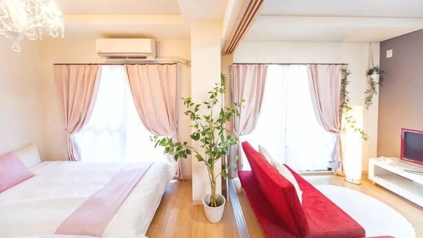 Habitación de hotel con dos camas, un televisor, una planta y un sofá rojo.