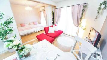 A modern hotel room with a bed, red sofa, dining table, and white chairs.