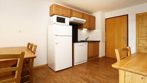 A compact kitchen with wooden cabinets, a white refrigerator, a microwave, and a dishwasher. - Apartment in Orcières with Ski Slope Access (Orcières)